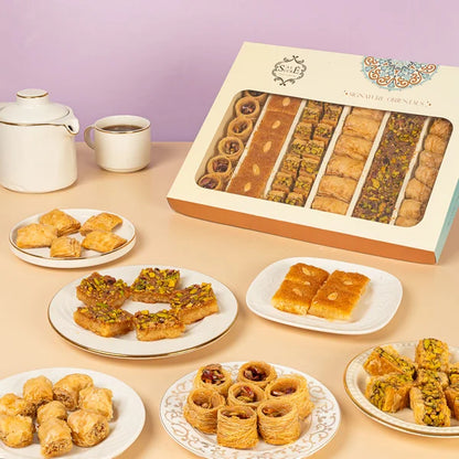 Assorted baklava and pastries displayed on plates with a box of baklava in the background. Salet_Sucre-Oriental_sweets ساليه سوكريه